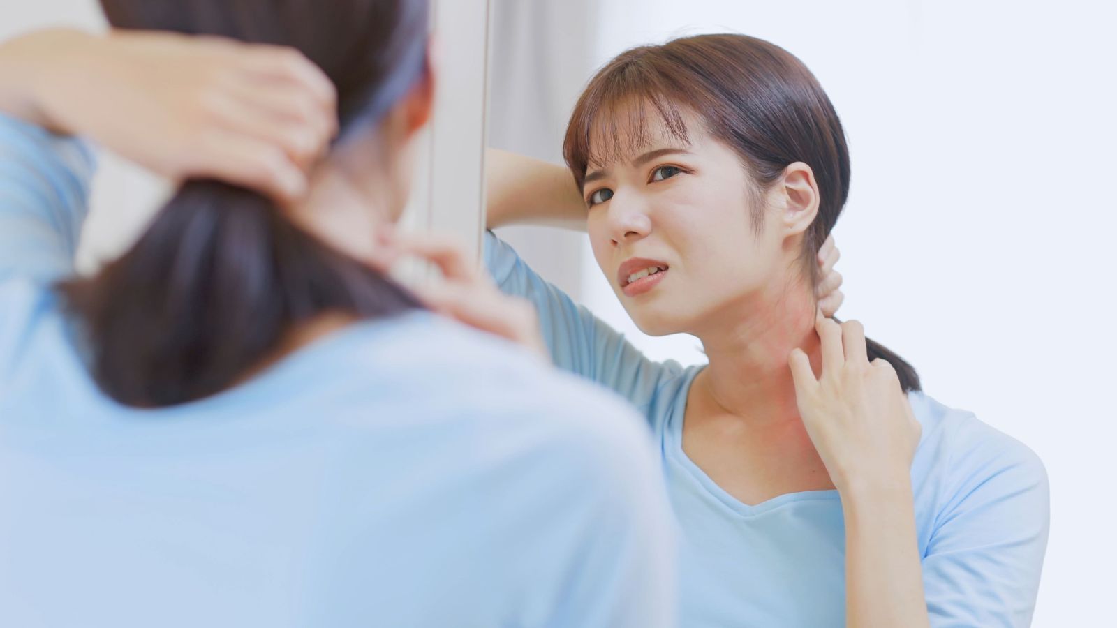 An Asian woman has skin allergies, so she scratches her neck in front of the mirror at home.